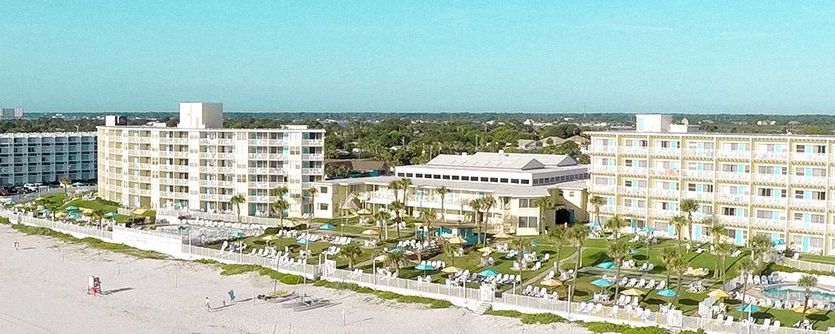 A wide-angle view of a large, multi-story hotel with a pool and beach in front of it.