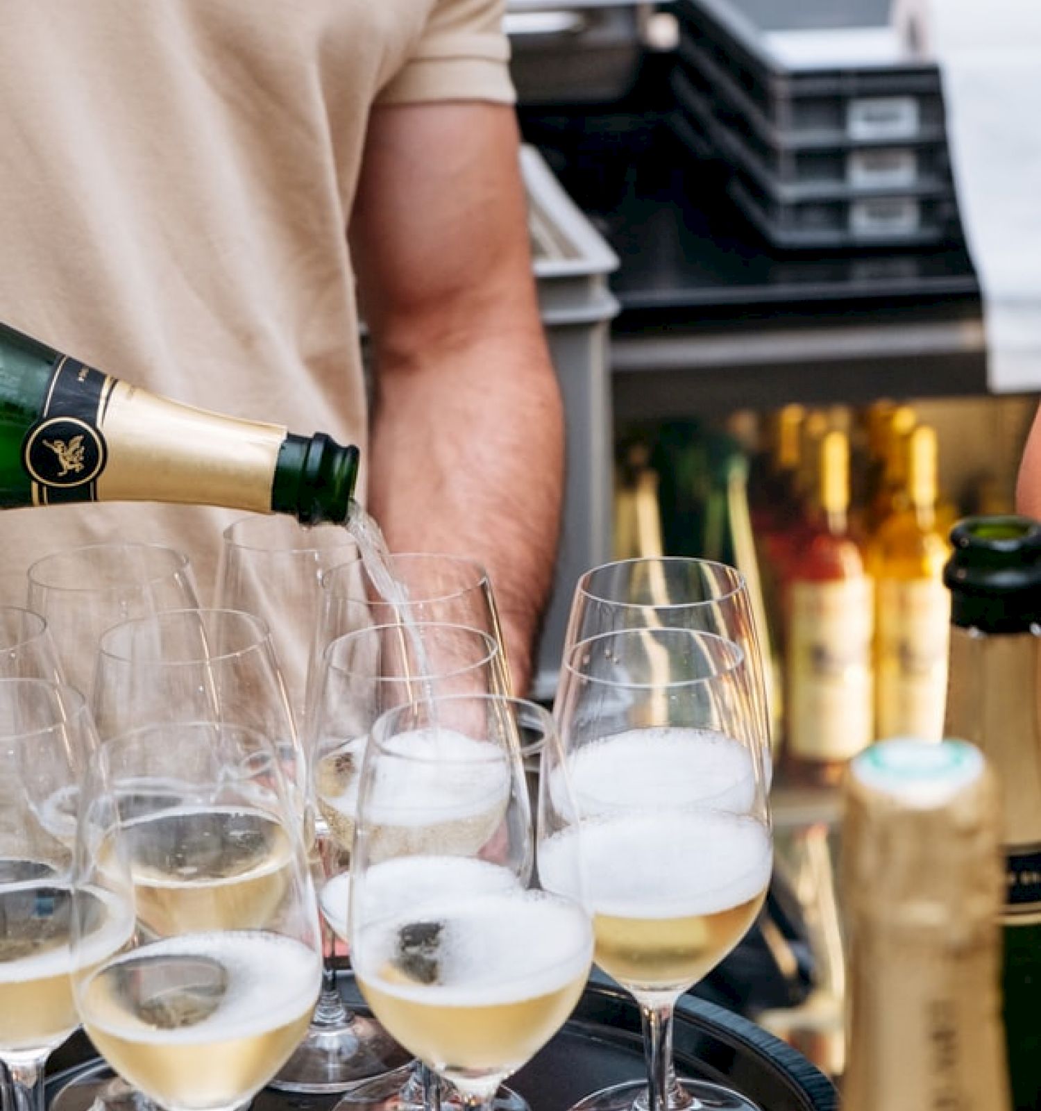 A person is pouring champagne into several glasses, with bottles and other items on a counter nearby. It appears to be a festive or celebratory setting.