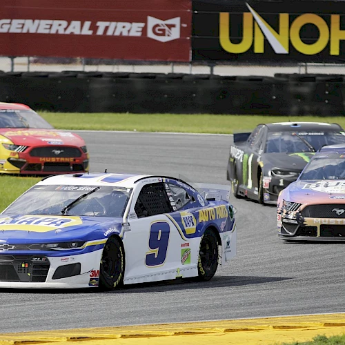 Several race cars compete on a track, including vehicles numbered 9 and 12, with advertisements in the background.