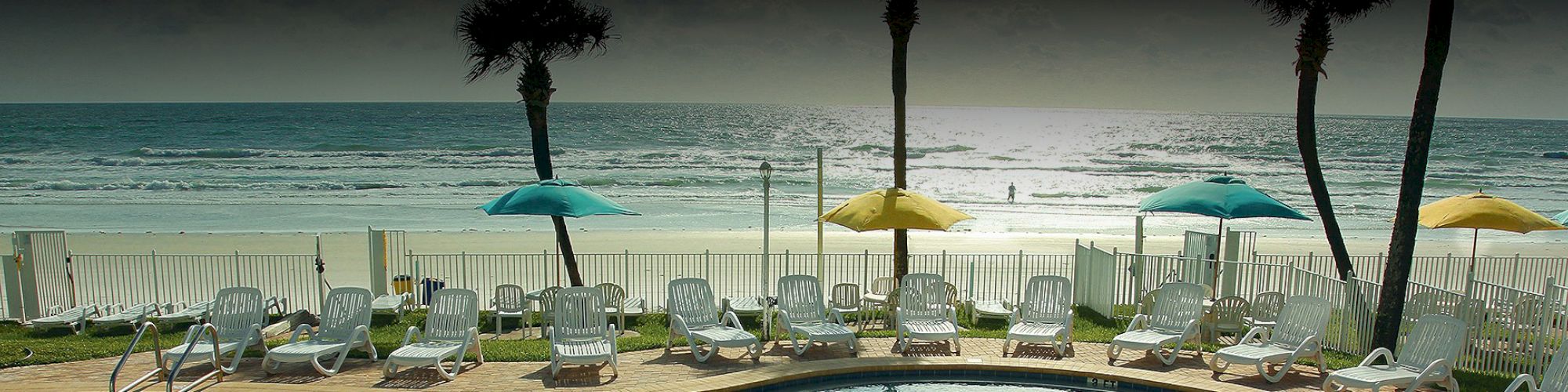 A serene beach scene featuring lounge chairs, colorful umbrellas, palm trees, and a gently rolling ocean.