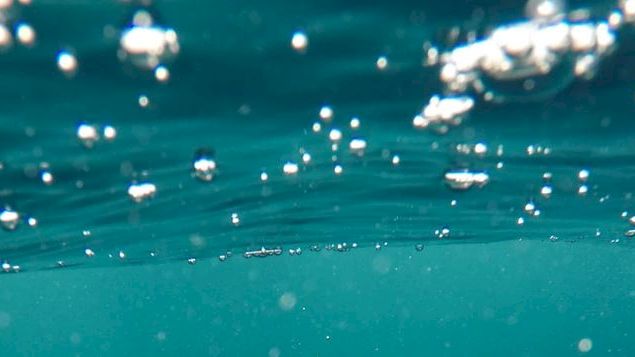 This image shows an underwater view with bubbles rising toward the surface of the ocean or a pool, giving a sense of being submerged.