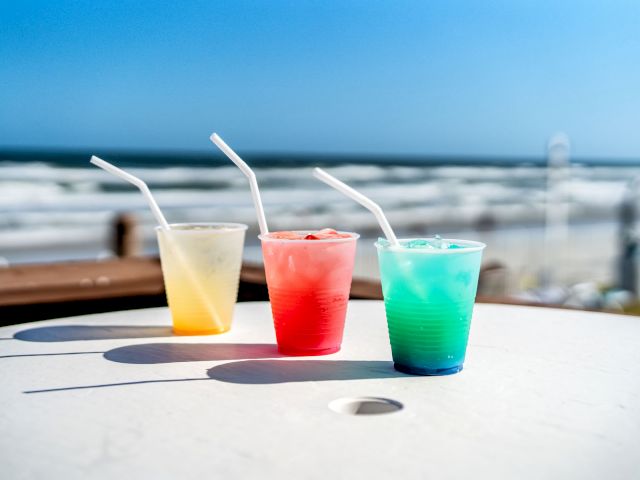 Three colorful drinks on a table with a beach and ocean in the background.