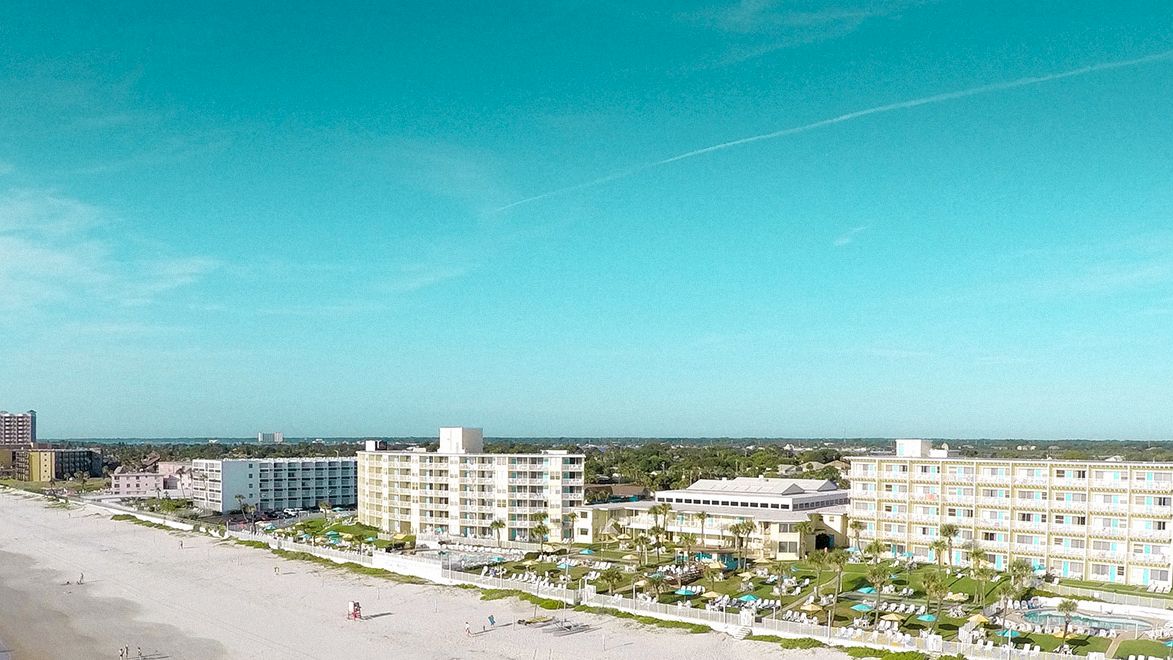 A wide-angle view of a beachfront resort with multiple buildings, pools, and palm trees.