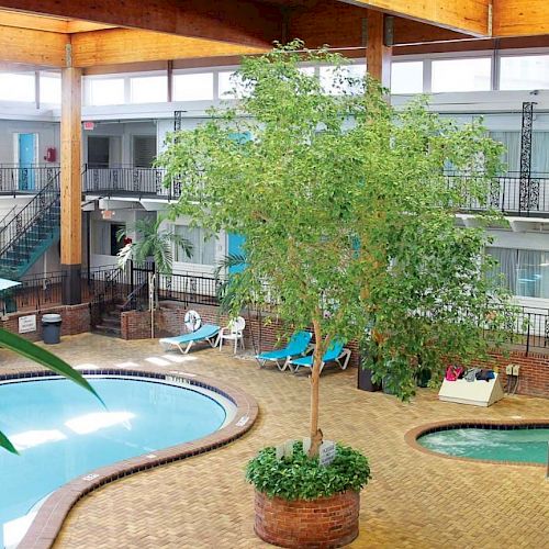 This image shows an indoor pool area with a tree in the center, surrounded by hotel rooms with blue doors, plants, and a hot tub.