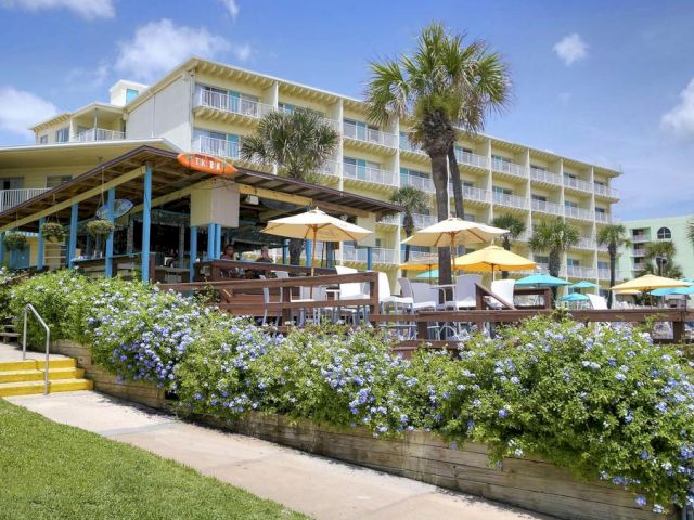 A full view of a multi-story hotel building with balconies, a patio area with umbrellas, and surrounding landscaping.