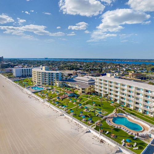 A beachside view with hotels, a swimming pool, and a clear blue ocean stretching into the horizon, under a partly cloudy sky.