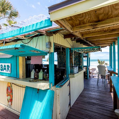 This image shows a beachside tiki bar with wooden decor, a palm tree, and an ocean view. The sign reads 