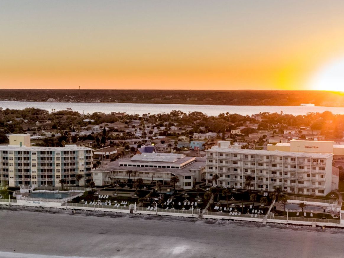 Aerial view of a beachfront resort with a pool and buildings at sunset.