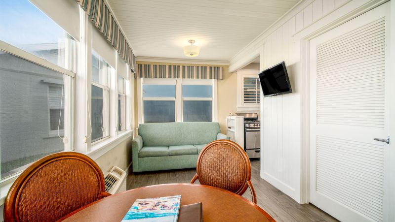 A brightly lit living area with a kitchenette, sofa, and dining table.