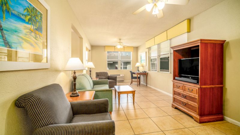 A wide view of a hotel room with a sofa, TV, coffee table, desk, and lamps.