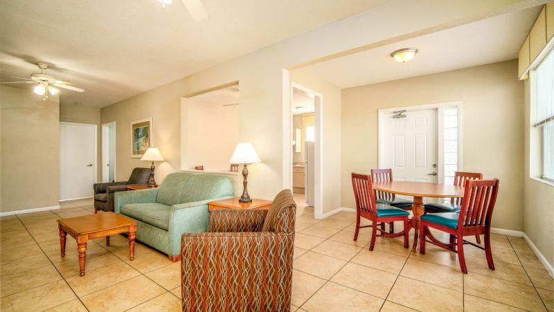 A wide view of a furnished living room and dining area with a sofa, coffee table, dining table, chairs, and lamps.