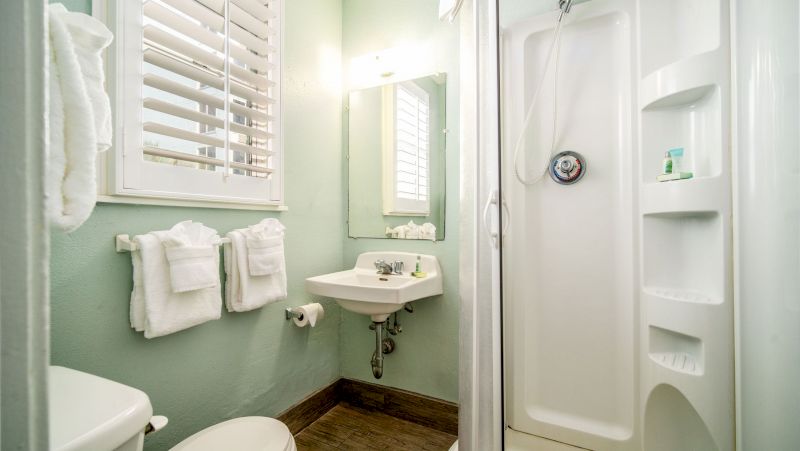 A bathroom with a toilet, shower, sink, towels, and mirror.