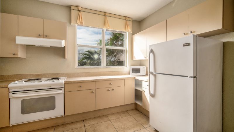 A kitchen with light-colored cabinets, white appliances, and a window above the counter.