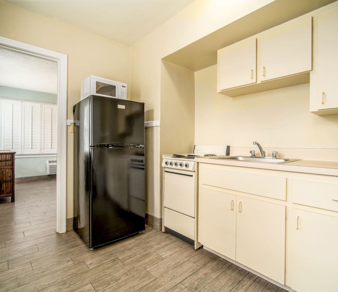 A kitchen with a black refrigerator, white stove, and sink with cream-colored cabinets.