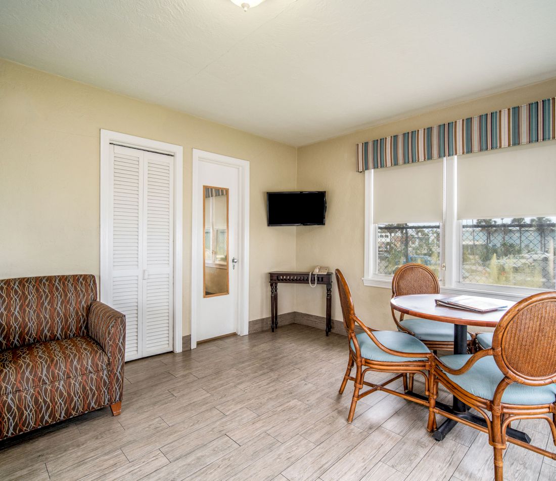 A wide view of a hotel room with a table, chairs, sofa, TV, and window
