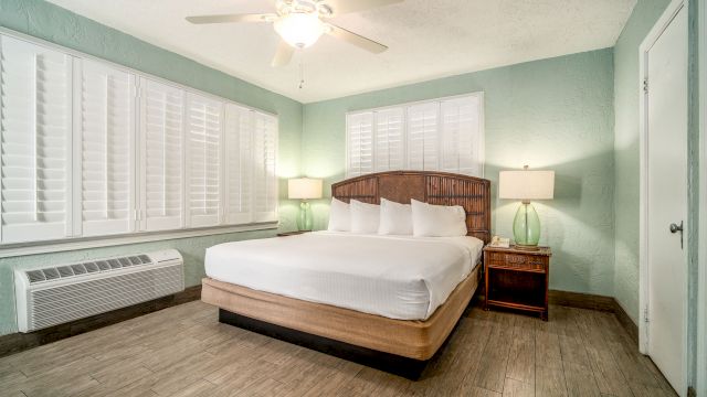 A wide-angle view of a hotel room with a large bed, two nightstands, and a window with white shutters.