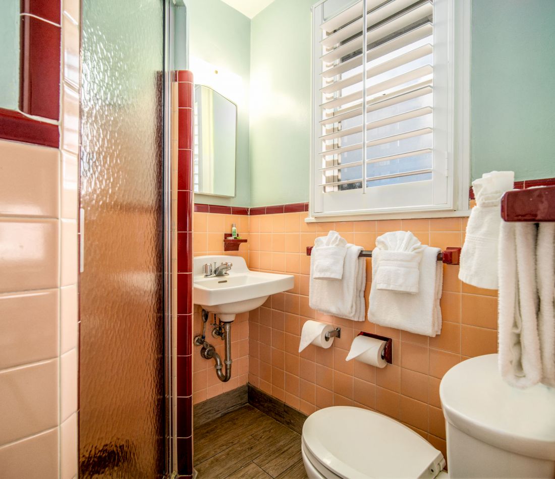 A bathroom with peach and red tiled walls, a white sink, toilet, and shower.