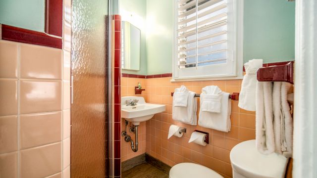 A bathroom with peach and red tiles, a shower, sink, toilet, and towels.