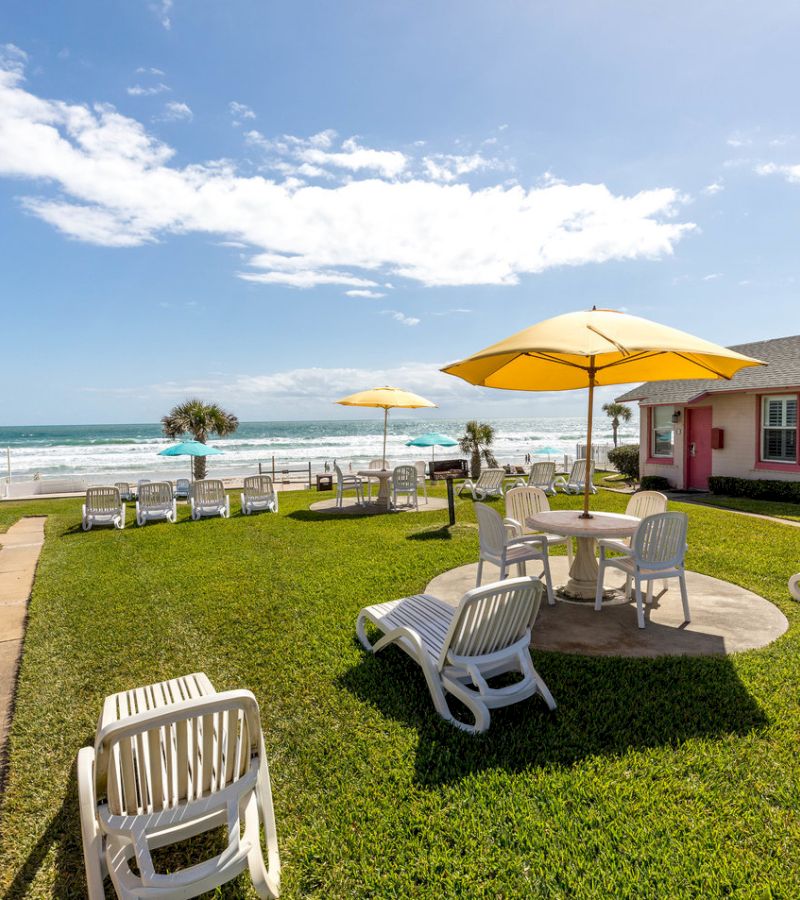 A beachside seating area with white plastic furniture and yellow umbrellas overlooking the ocean.