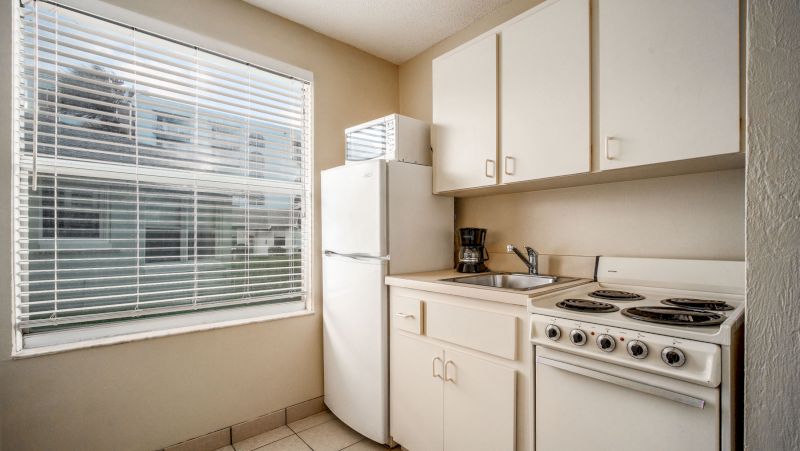 A small kitchenette with white appliances and a window with blinds.