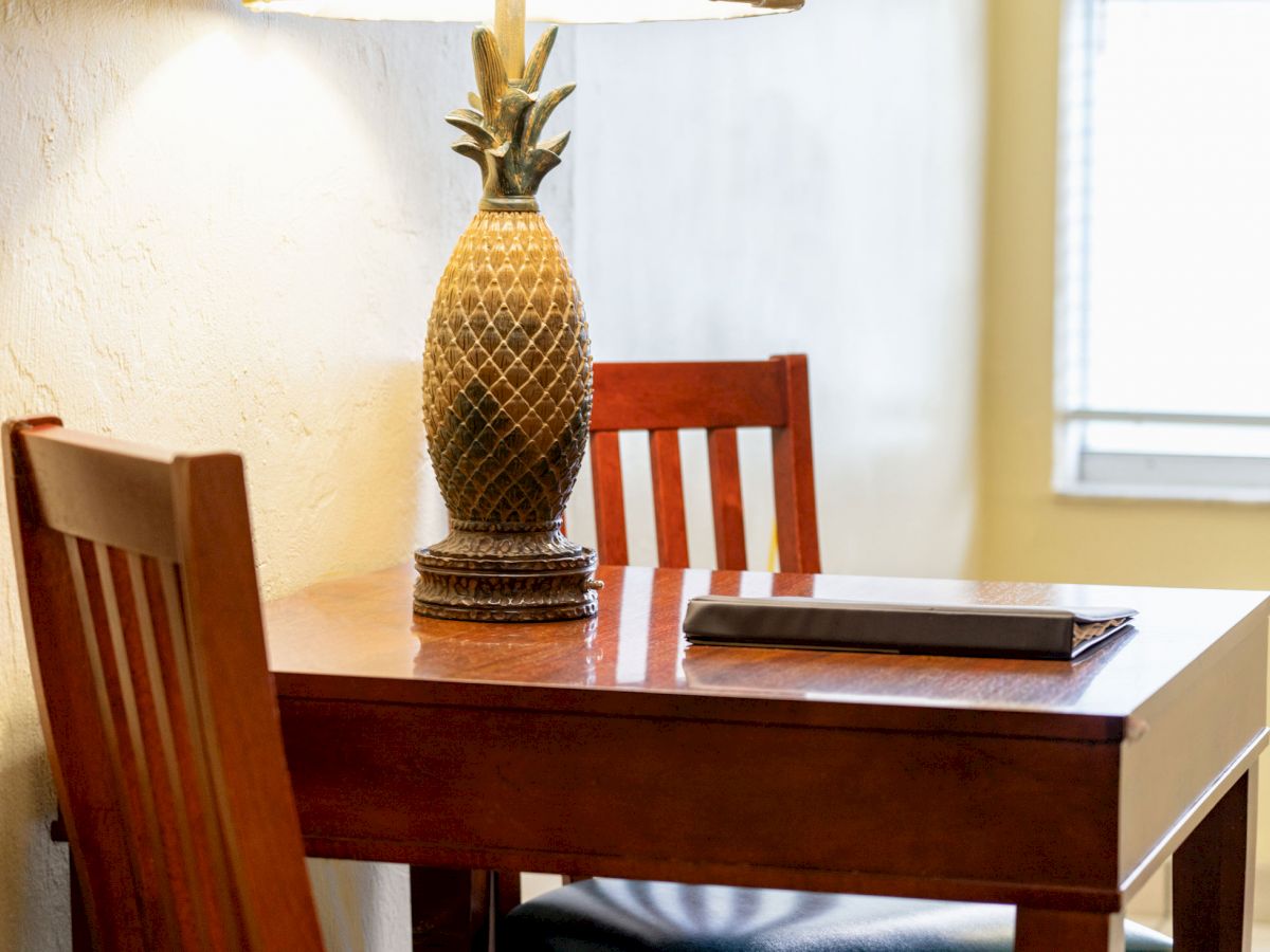 A small wooden desk with a matching chair, a pineapple-shaped lamp, and a closed book under soft indoor lighting.