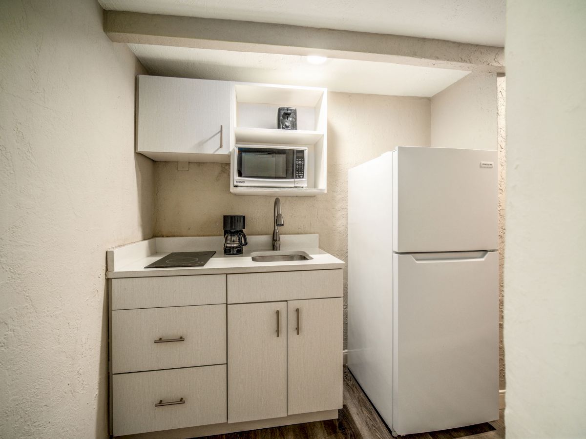 A small kitchen area with a refrigerator, microwave, coffee maker, sink, and cabinets in a compact space.