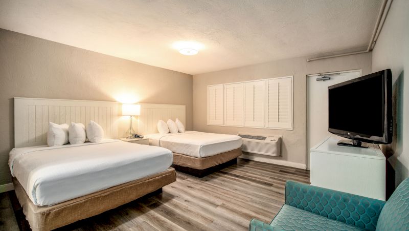 A hotel room with two double beds, a flat-screen TV on a white cabinet, and a window with white shutters.