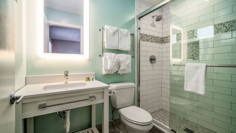 A clean bathroom with a toilet, shower, sink, and mirror.