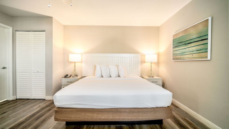 A wide view of a hotel room with a bed, nightstands, lamps, and artwork.