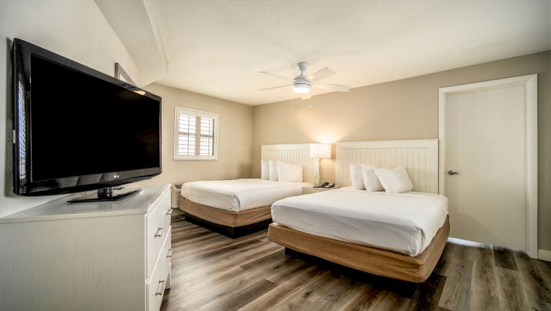 A hotel room with two beds, a TV, and a ceiling fan.