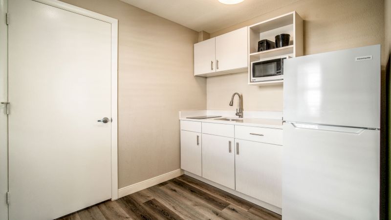 A compact kitchenette with white cabinets, a microwave, sink, and refrigerator.