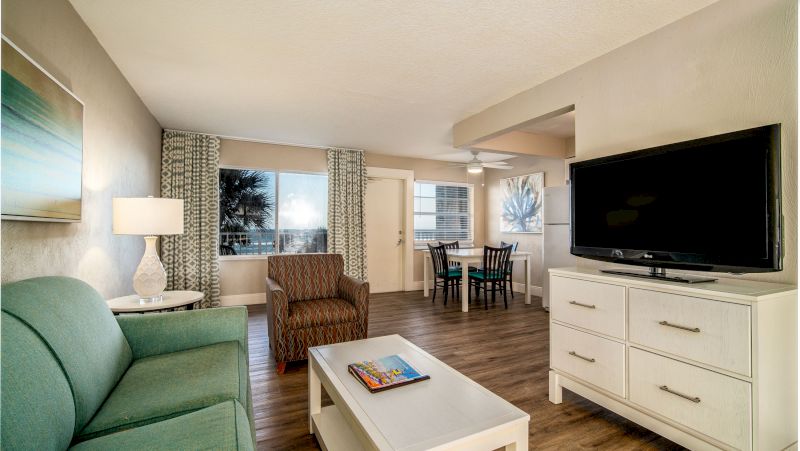 A wide view of a living room with a sofa, armchair, coffee table, TV, and dining table.