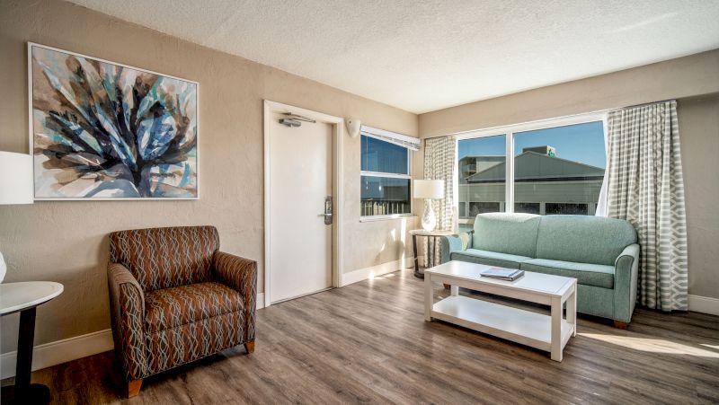 A furnished living room with a sofa, armchair, coffee table, and artwork on the wall.