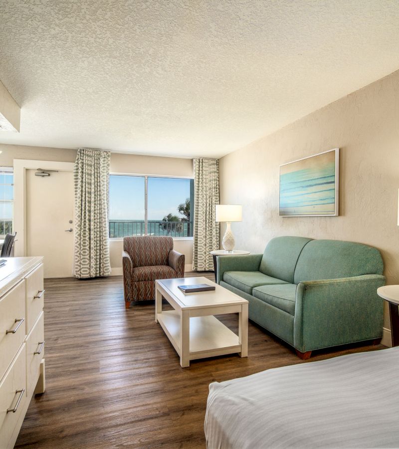 A wide view of a hotel room's living area with a sofa, armchair, coffee table, and window