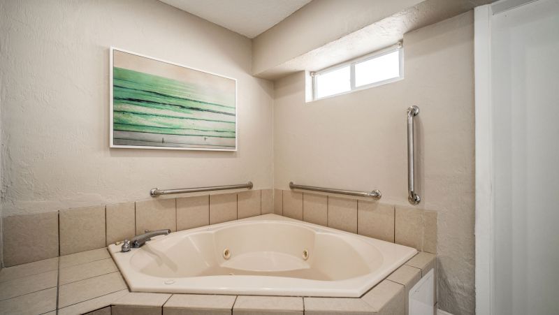 A beige bathroom with a large jacuzzi tub, tile surround, handrails, and artwork on the wall.