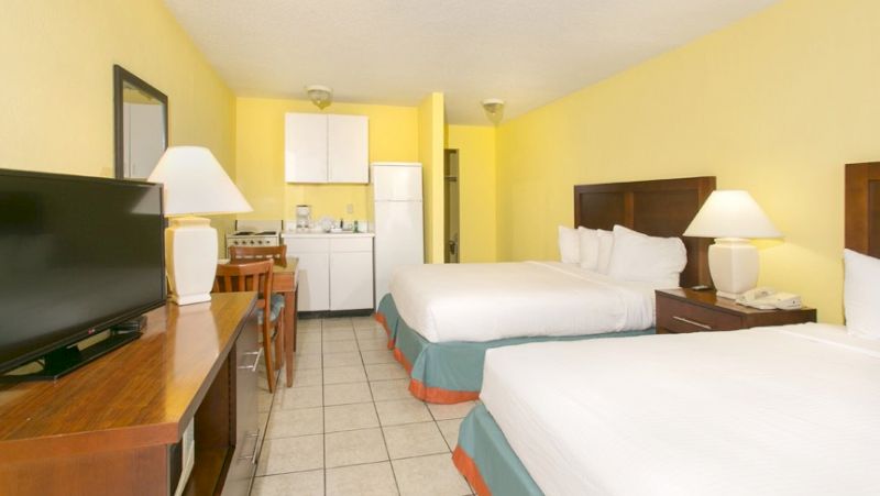 A wide view of a motel room with two double beds, a kitchenette, and a TV on a stand.