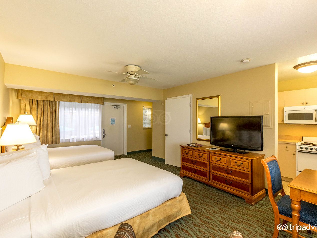 A wide view of a motel room with two beds, a TV, a kitchenette, a dresser, and a table with chairs.