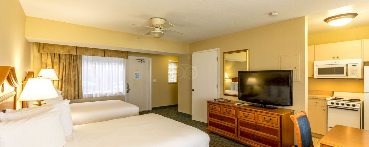 A hotel room with two double beds, a kitchenette, and a TV on a dresser.
