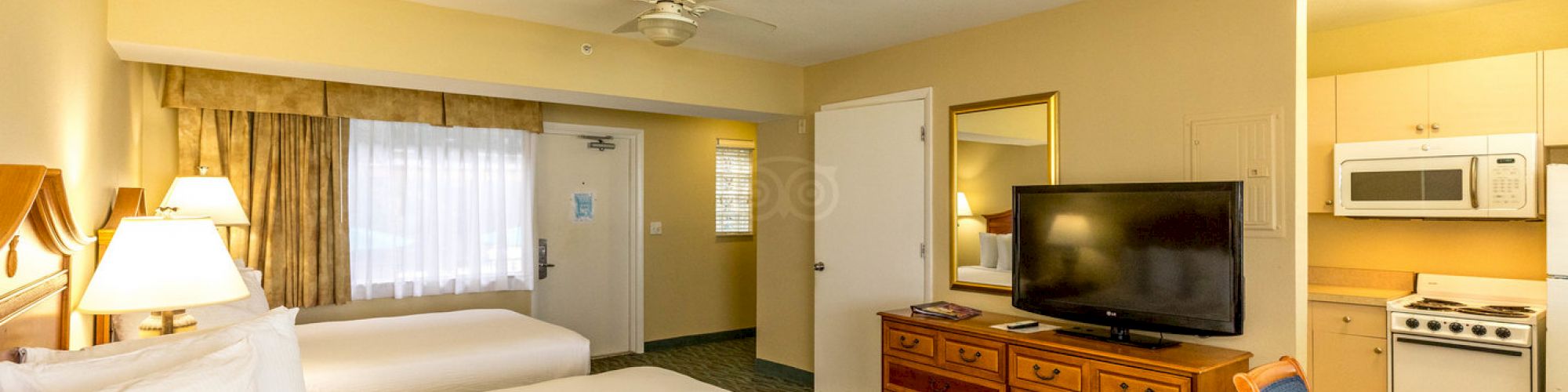 A hotel room with two beds, a TV, a desk, a microwave, and a refrigerator, with the door leading to the outside.