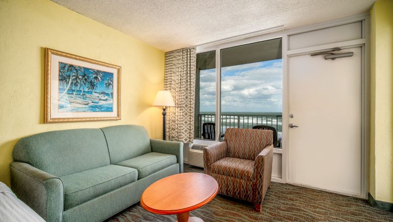A hotel room living area with a sofa, chair, coffee table, and lamp.