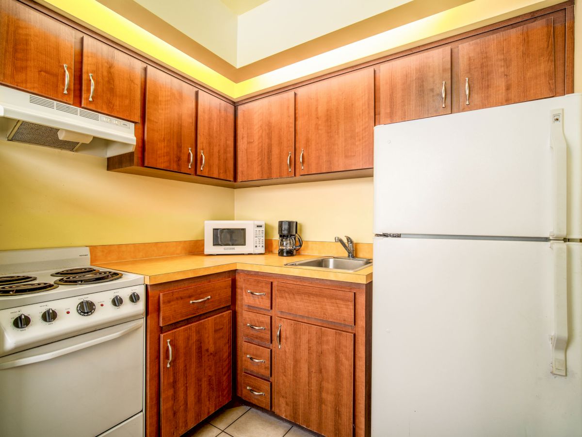 A compact kitchen with wooden cabinets, a white refrigerator, stove, microwave, and coffee maker. The countertops are clean and tidy.