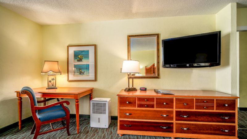 A hotel room with a desk, dresser, TV, and chair.