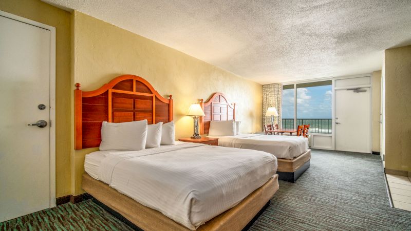 A hotel room with two beds, a nightstand, and a balcony.