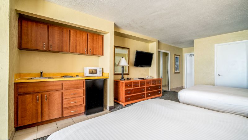 A hotel room with a kitchenette, two beds, and a TV