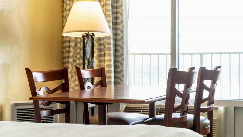 A hotel room with a dining table and chairs in front of a window with a balcony.