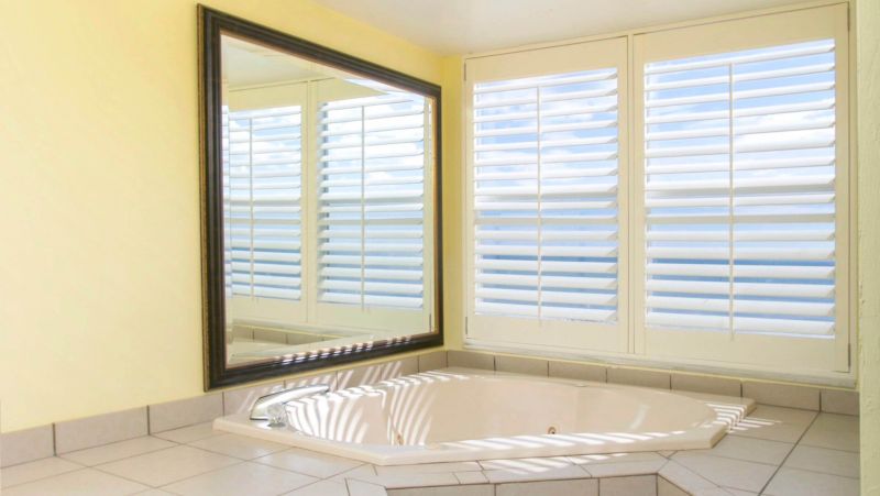 A bathroom with a large mirror, a jacuzzi tub, and a window with white blinds.