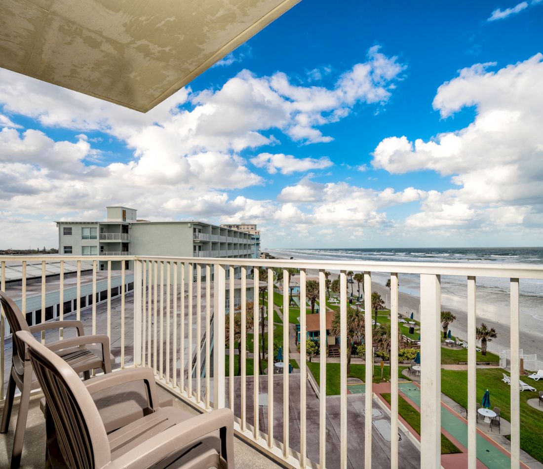A balcony with a white railing and plastic chairs overlooking the ocean and beach.