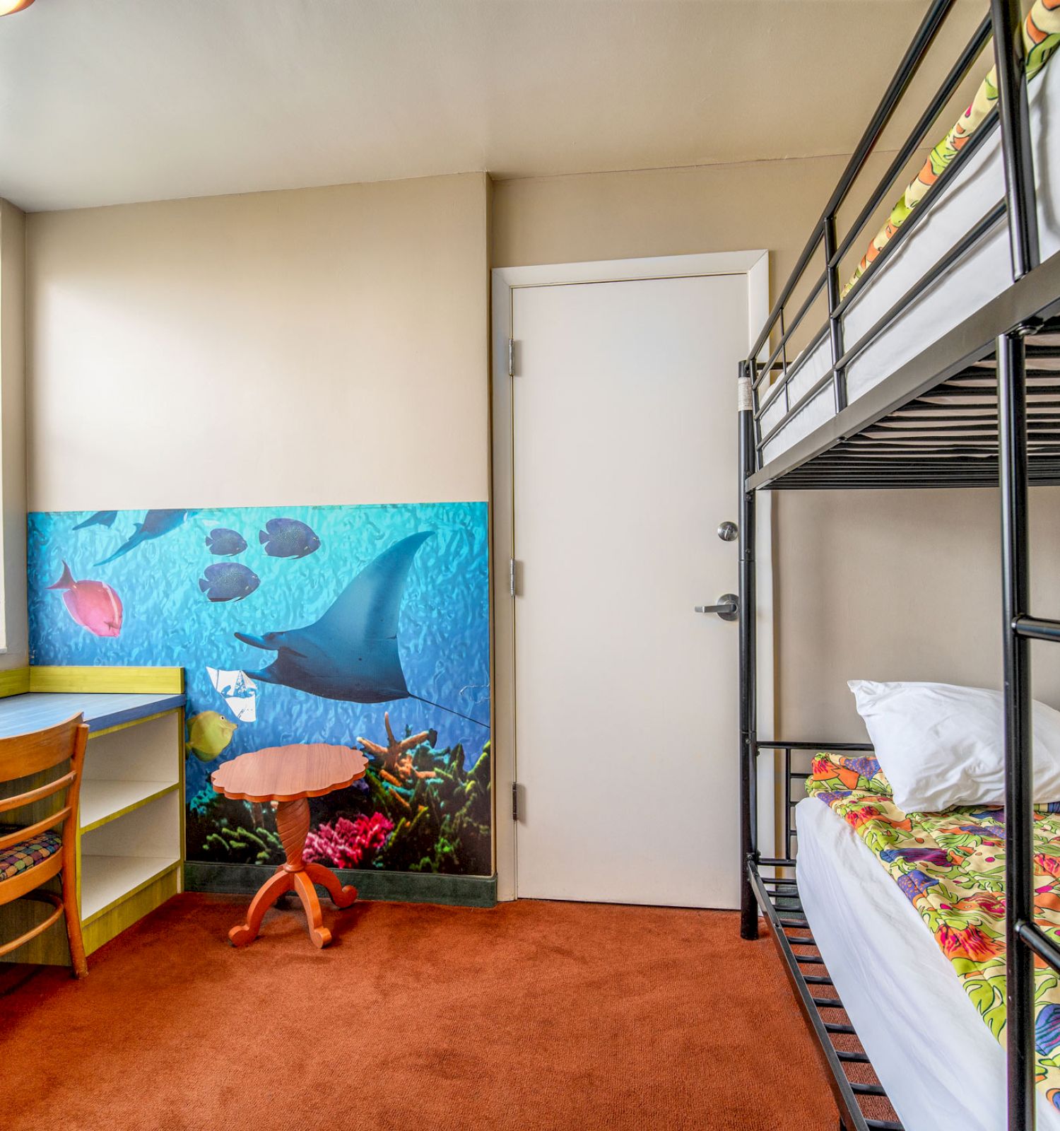 A colorful children's room with bunk beds, ocean-themed wall art, a window, a desk with a chair, and an orange carpet, ending the sentence.