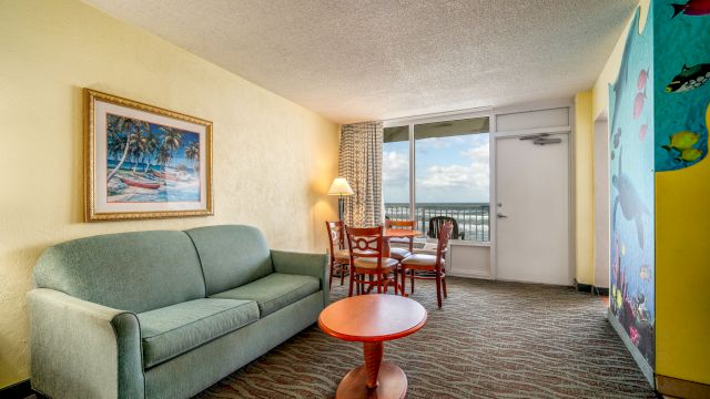 A living room with a sofa, coffee table, dining table, and balcony door.