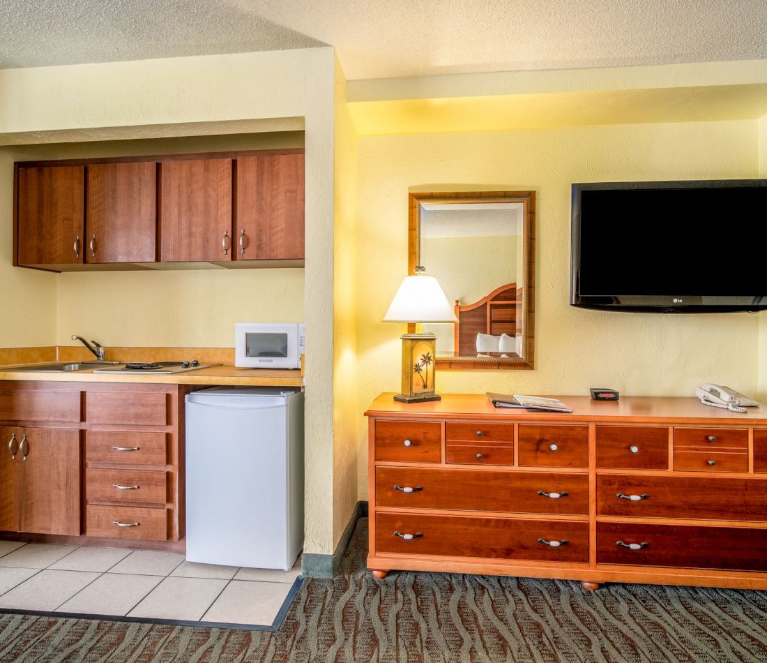 A hotel room with a kitchenette, dresser, and TV
